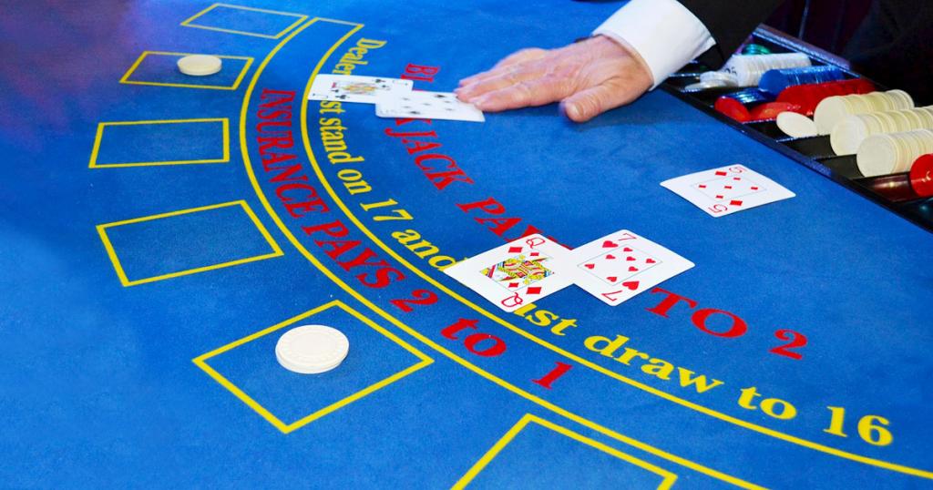 Auf dem Bild ist ein Black Jack-Spieltisch zu sehen. Der Dealer händigt gerade zwei Karten aus. Insgesamt nehmen zwei Spieler an dem Spiel teil.